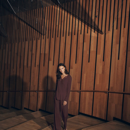Woman wearing vivid brown Lilith Pajama Set standing in a room with wooden paneling.