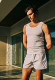 Man standing outside wearing Cotton Essentials Tank Top in white, paired with boxer shorts.