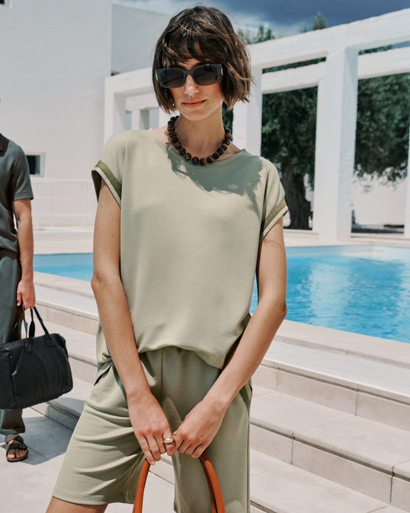 Woman in a green outfit standing by a pool with sunglasses on
