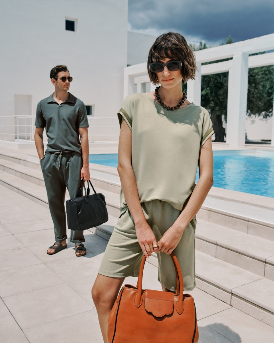 Woman holding a brown handbag with a man standing behind her by a pool.
