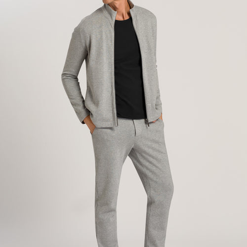 Man wearing a gray zip-up jacket and pants with a black shirt on a light gray background