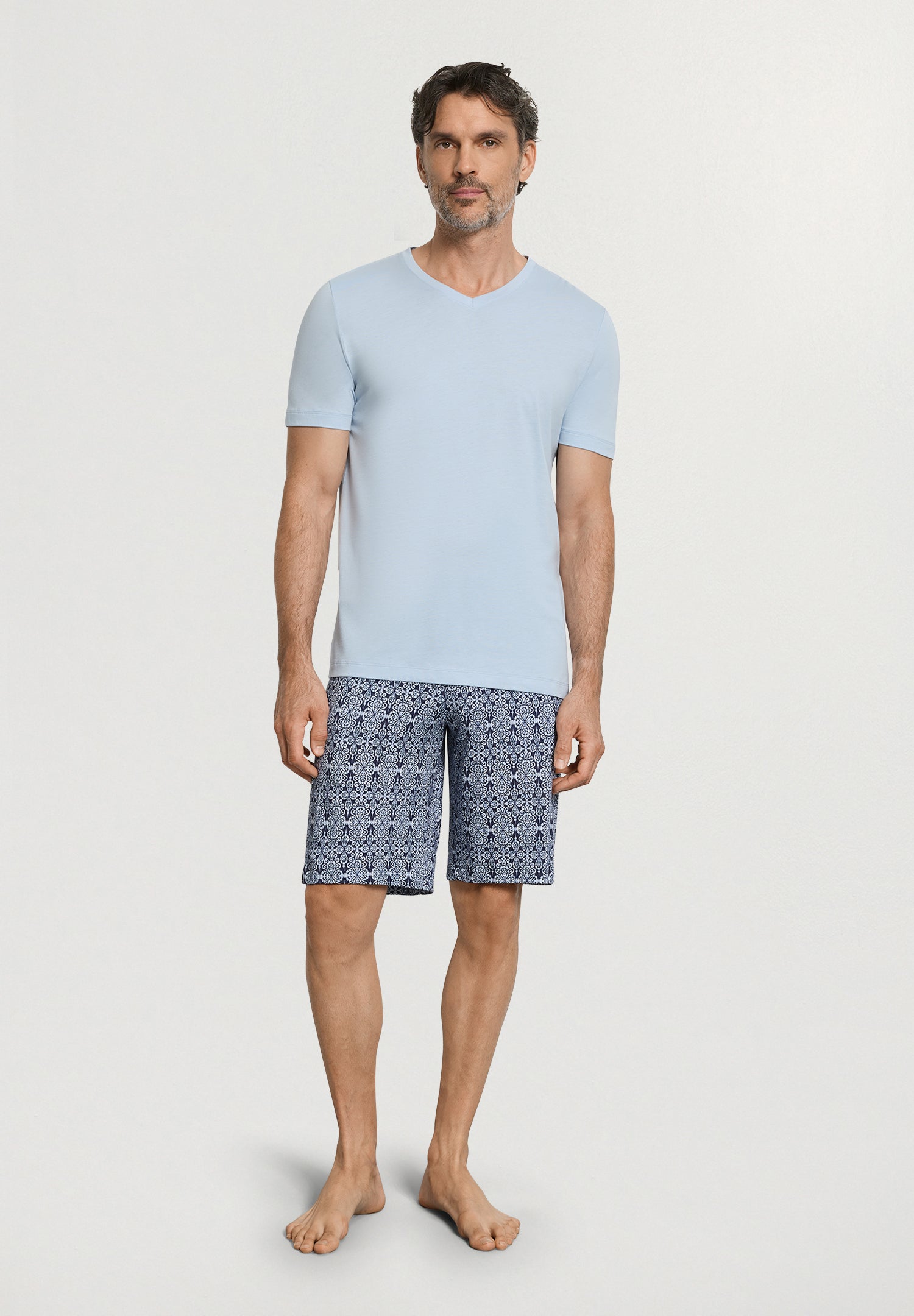 Man wearing a light blue t-shirt and patterned shorts on a white background