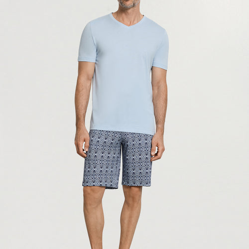 Man wearing a light blue t-shirt and patterned shorts on a white background