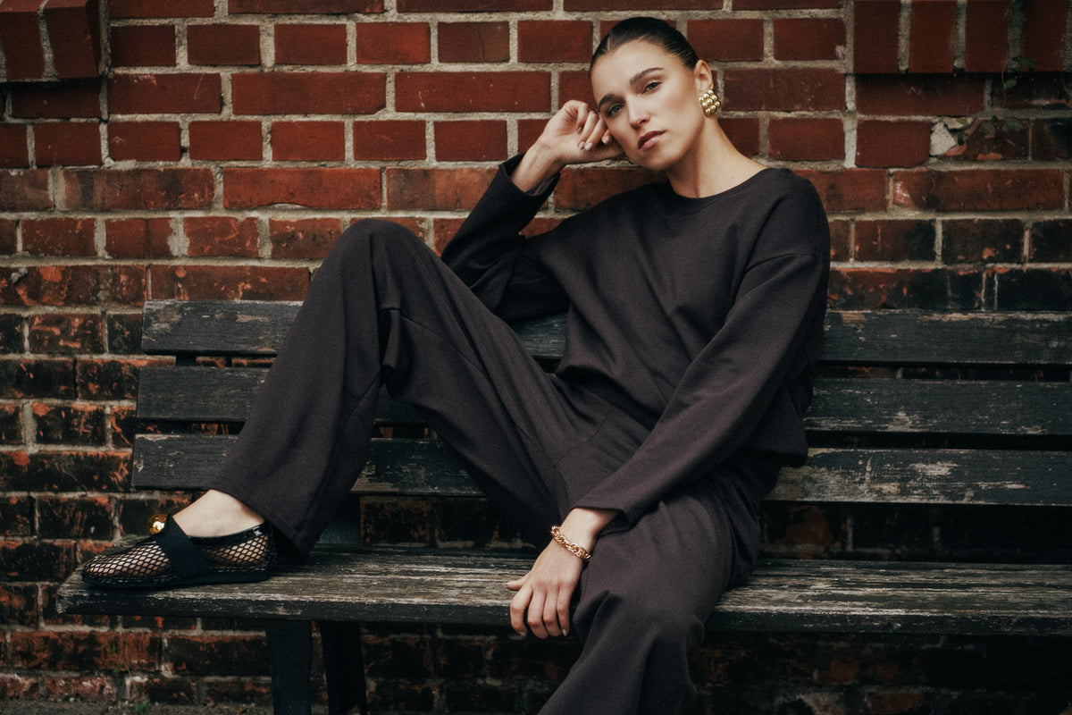 model posing on outdoor bench against brick wall, wearing brown Natural Living set