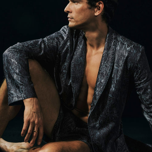 Man wearing a dark patterned robe against a black background