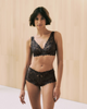 Woman wearing a black pearl Luxury Moments lingerie set against a beige background