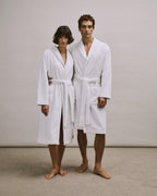 Woman and man wearing white  bathrobes from the Robe Selection Collection standing against a plain background