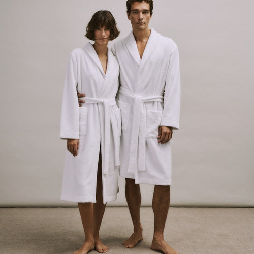 Woman and man wearing white  bathrobes from the Robe Selection Collection standing against a plain background