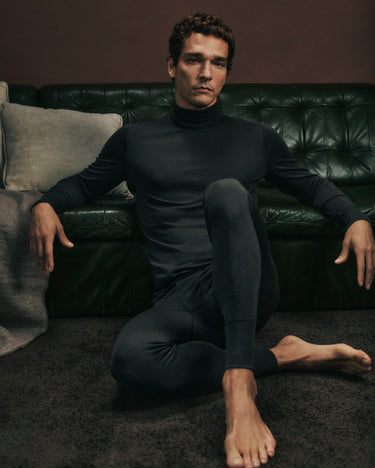 Man wearing a Earthy Ink wool turtleneck and wool leggings sitting on the floor in front of a dark leather couch.