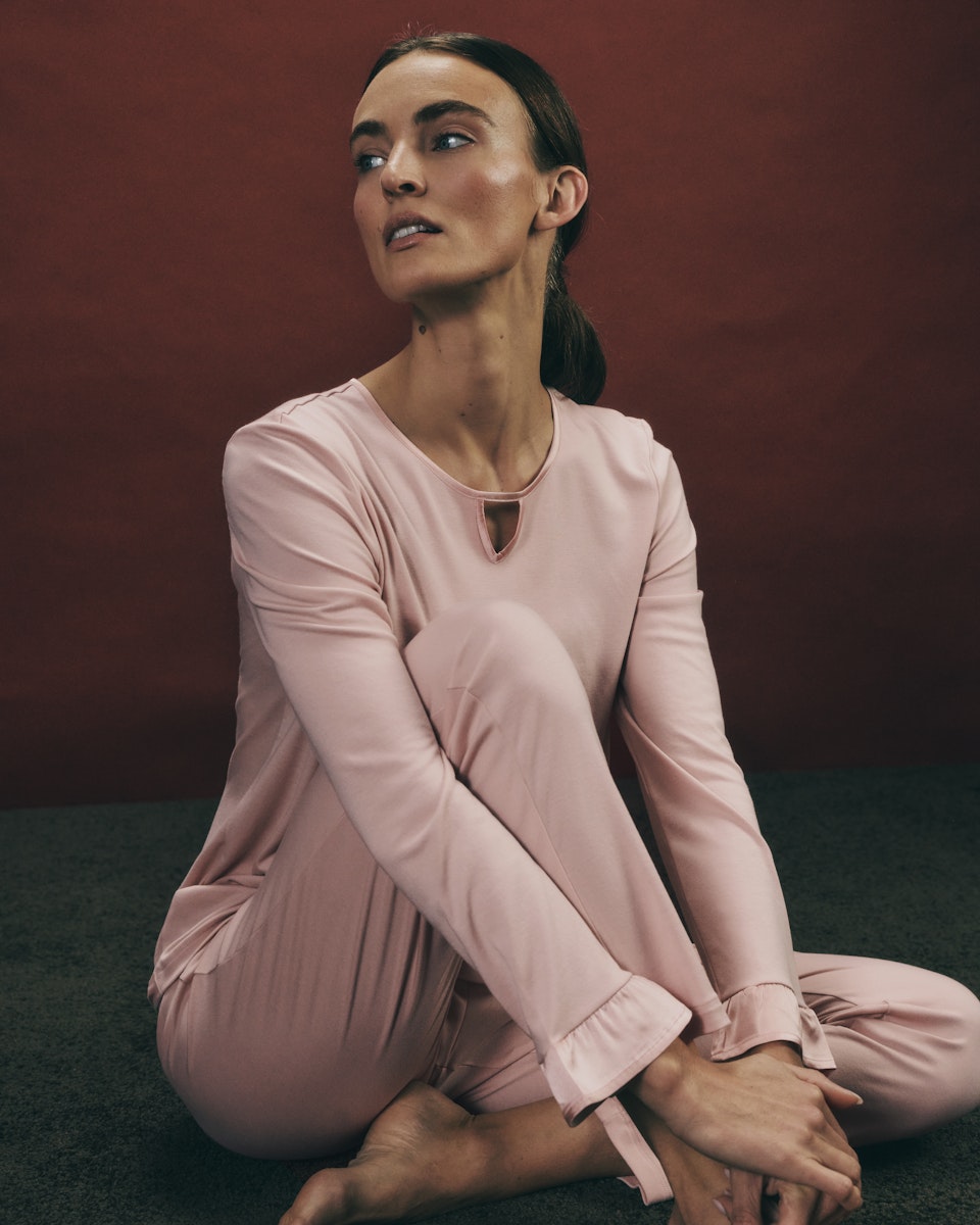 Woman wearing the Claire Cotton Pajama Set in blush pink sitting on the floor against a dark background