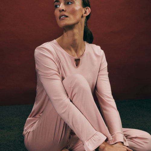 Woman wearing the Claire Cotton Pajama Set in blush pink sitting on the floor against a dark background