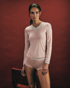 Woman wearing Dana blush pink long-sleeve top and boyleg with lace details against a red background