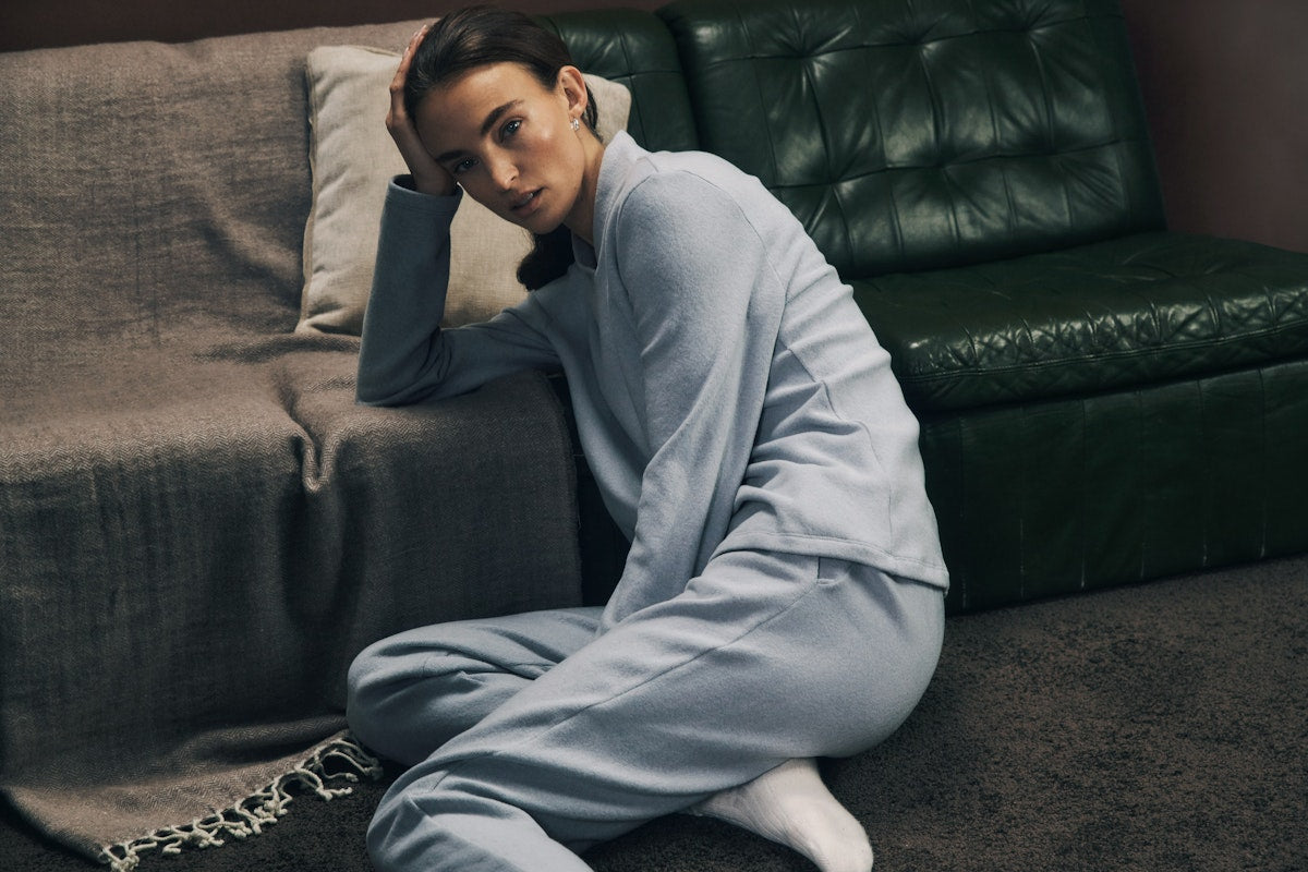 Person wearing a light blue tracksuit sitting on the floor against a dark green couch.