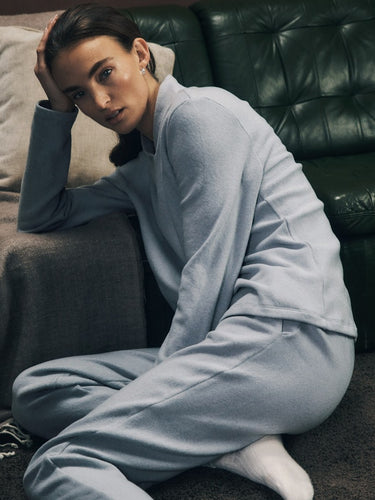 Person wearing a light blue tracksuit sitting on the floor against a dark green couch.