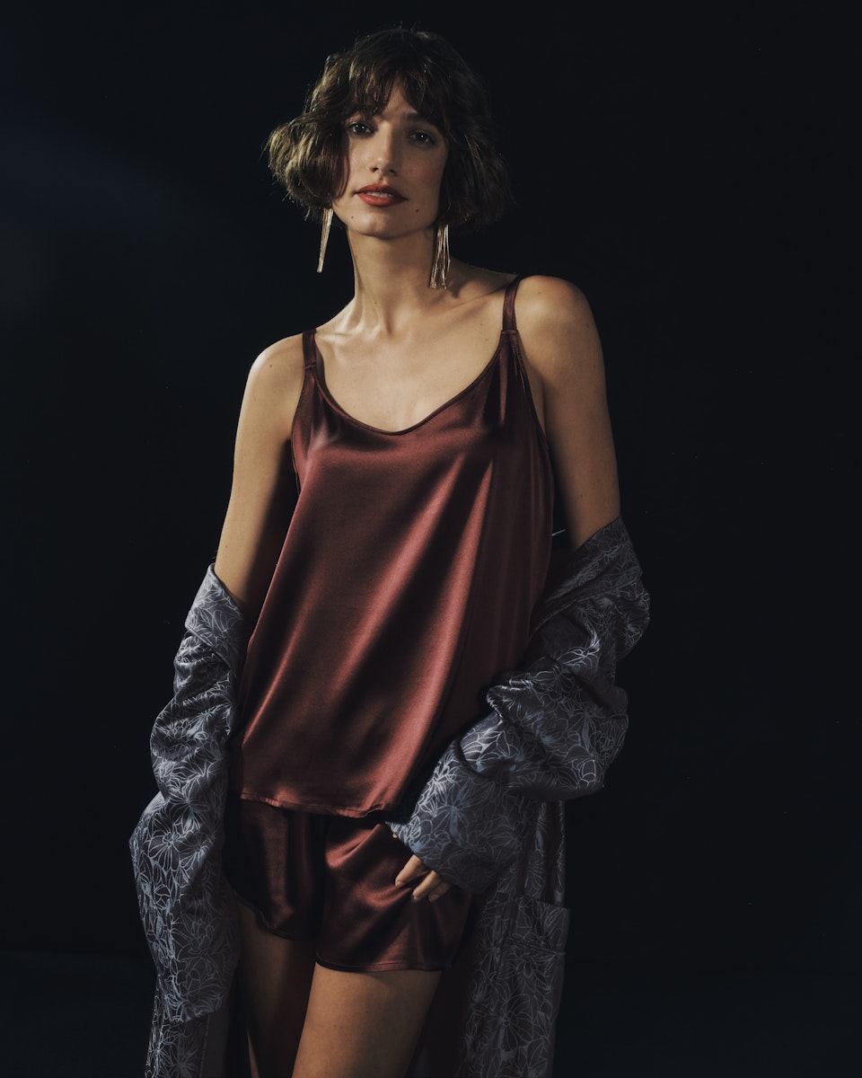Woman wearing Grand Central Silk Camisole and Knickers in vivid brown with men's Selection robe falling off the shoulders