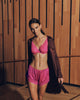 Woman wearing a pink Lilith bra and knickers with a vivid brown robe standing in front of a wooden paneled wall.