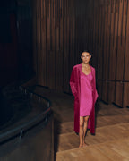 Woman wearing Lilith pink dress and Favourites robe standing in a dimly lit room with wooden walls.