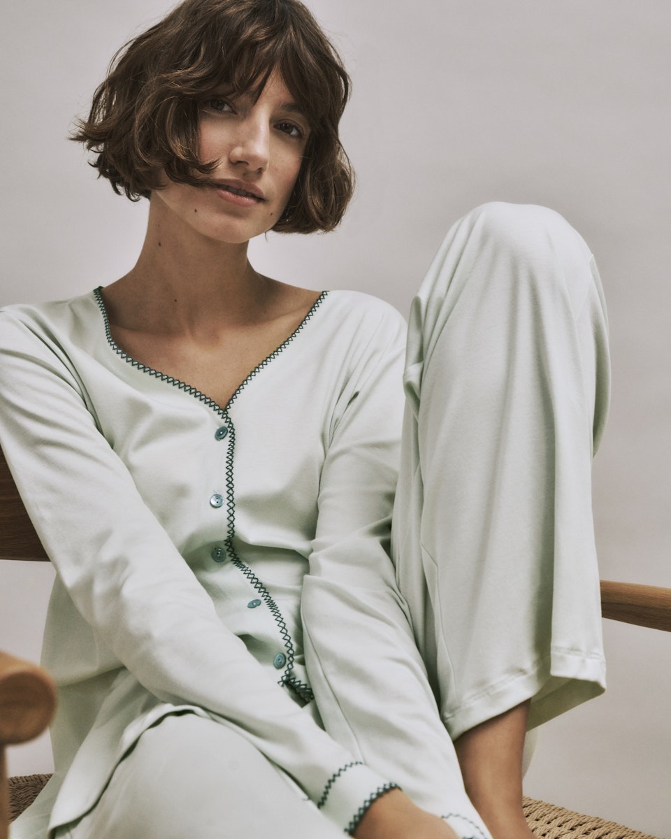 Woman wearing a light green Una pajama set sitting on a chair.