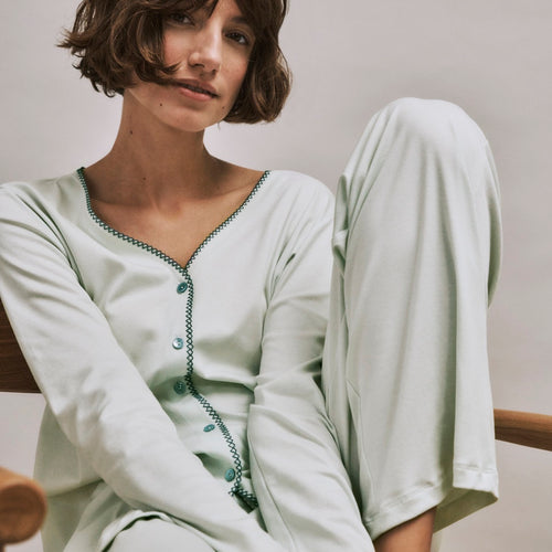 Woman wearing a light green Una pajama set sitting on a chair.