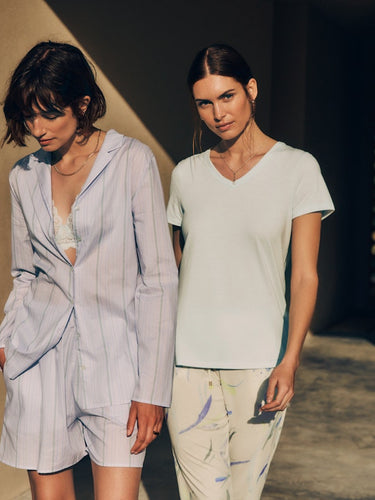 Two women standing together. The women on the left is wearing Sleep And Lounge Cotton Button Front Pajama Shirt in Pastel Dream  over Luxury Moments Lace Soft Cup Bra in Vapor  and Sleep And Lounge Relaxed Cotton Shorts Pastel Dream. The women on the right is wearing Sleep And Lounge Relaxed V-Neck T-Shirt in Vapor paired with Sleep And Lounge Cotton Blend Drawstring Pants in Dive Of Color