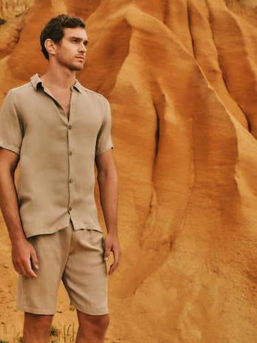 Man standing in front on sand dunes, wearing the Urban Casuals Button Front Shirt and Shorts in Savanna