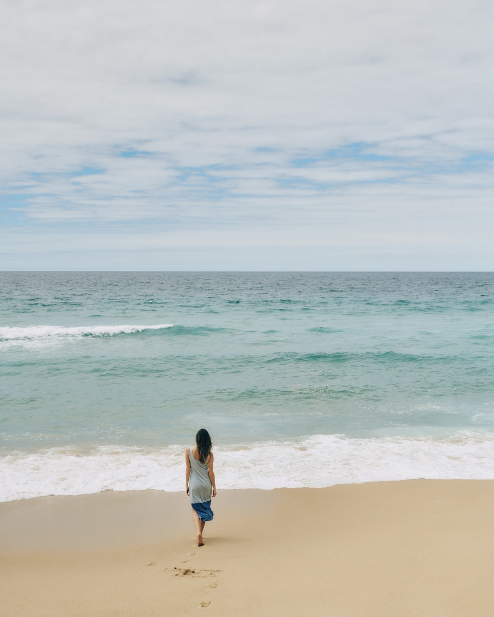 Woman wearing the Laura Long Tank Dress in Sea Breeze, walking toward the ocean.