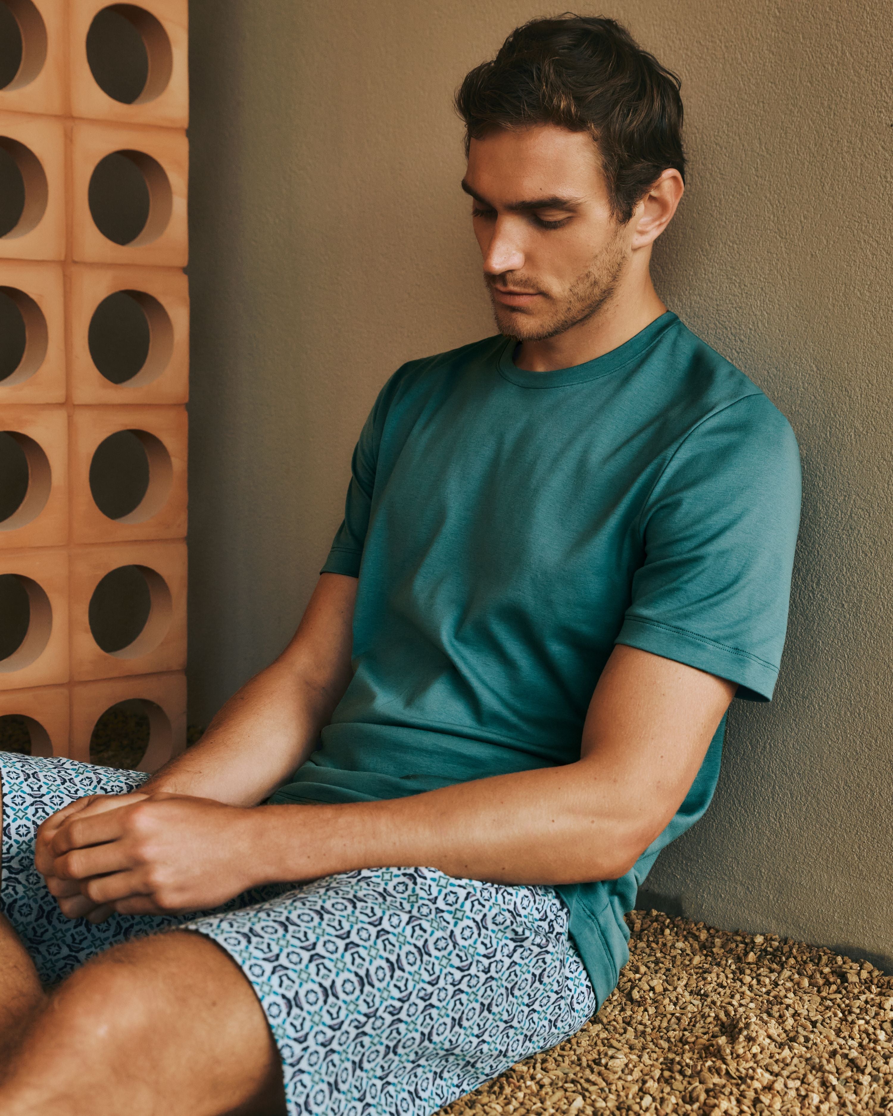 Man sitting on the ground, wearing the Night and Day Short Sleeve Pajama Set in Tinted Mosaic