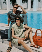 Man and woman sitting by a poolside with sunglasses and handbags.