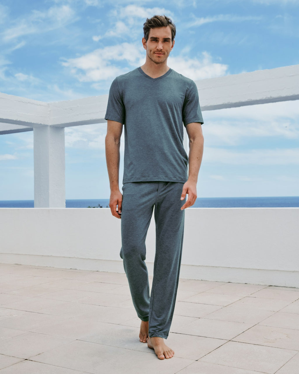 Man wearing a blue pajama set on a rooftop with a blue sky and ocean view.