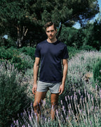 Man standing in a lavender field wearing a navy t-shirt and patterned shorts.