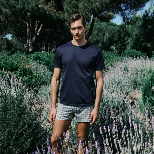Man standing in a lavender field wearing a navy t-shirt and patterned shorts.