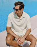 Man in a white polo shirt and shorts sitting by a pool