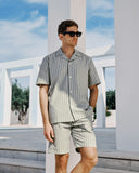 Man wearing a striped shirt and shorts standing in front of white columns with a blue sky.