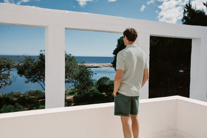 Man standing on a balcony overlooking a scenic view of water and trees.