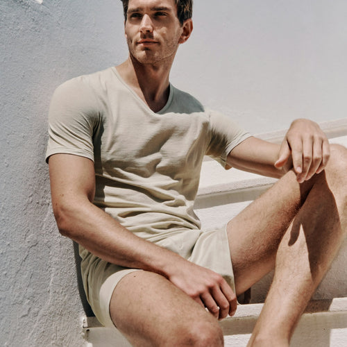 Man sitting on a staircase wearing a beige t-shirt and shorts.