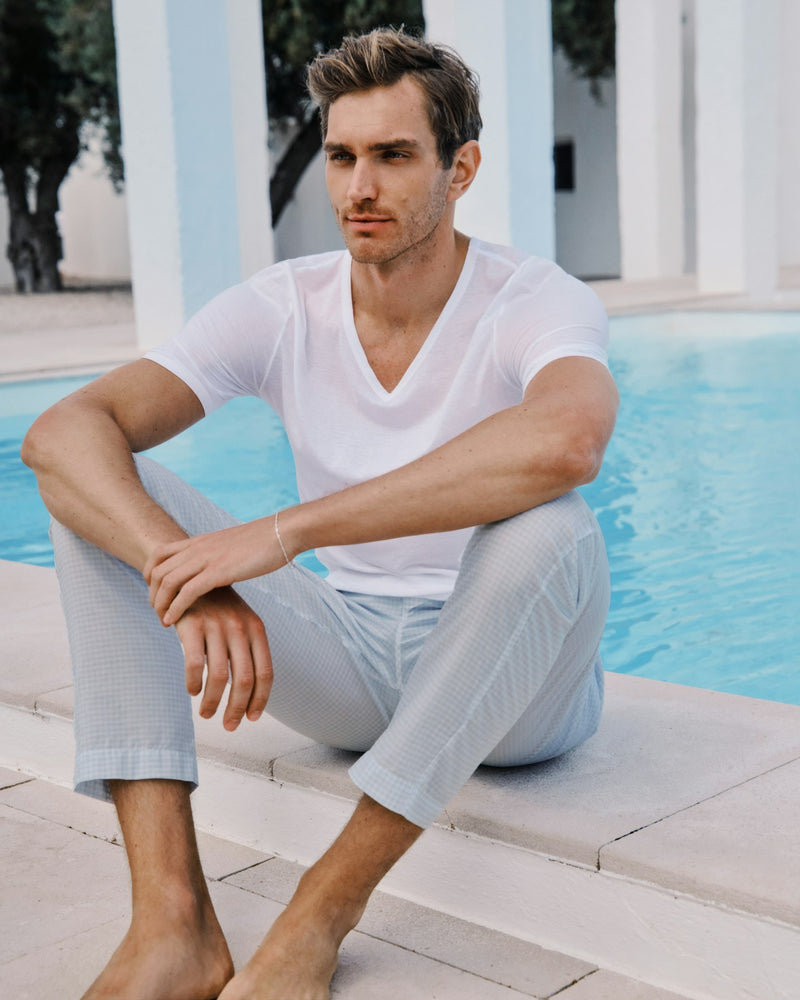 Man sitting by a pool wearing a white t-shirt and light blue pants.