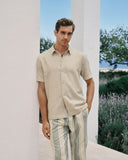 Man wearing a beige shirt and striped pants standing in a scenic outdoor setting with lavender.