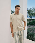 Man wearing a beige shirt and striped pants standing in a scenic outdoor setting with lavender.