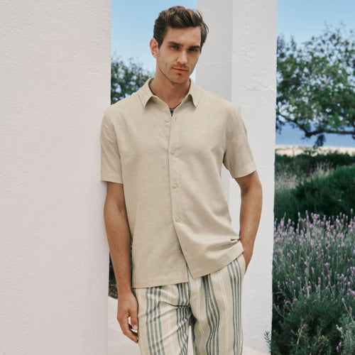 Man wearing a beige shirt and striped pants standing in a scenic outdoor setting with lavender.