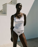 Woman wearing a white swimsuit with lace details against a light background