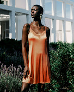 Woman wearing an orange dress standing outdoors with greenery and a building in the background