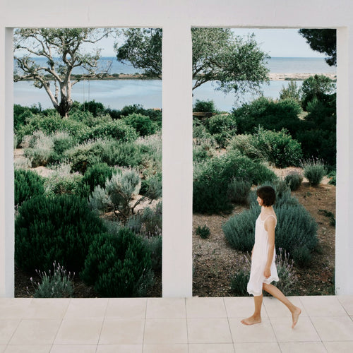 Woman walking on a path with a scenic view of trees and water through large windows.