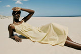 Woman in a yellow dress lying on sand with a clear blue sky