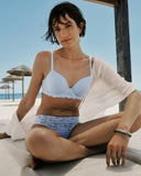Woman in a light blue bikini sitting on a beach with umbrellas in the background