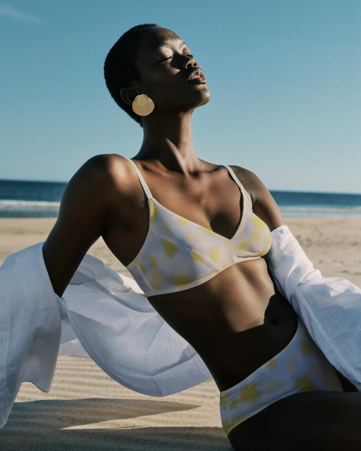 Woman in a yellow polka dot bra and underwear on a beach with ocean and sky in the background