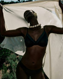 Person wearing a black bikini with a white fabric draped over them, standing outdoors.