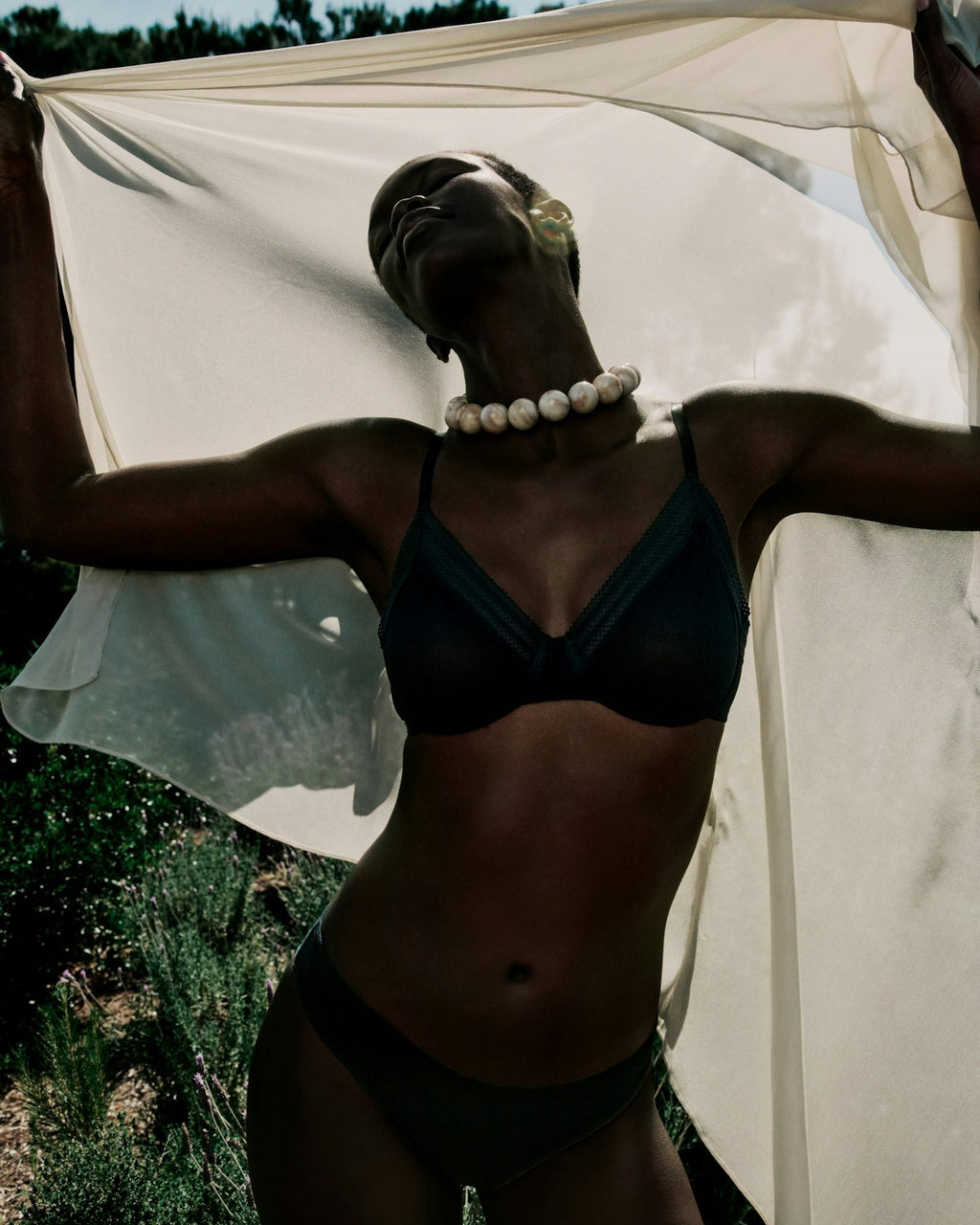 Person wearing a black bikini with a white fabric draped over them, standing outdoors.