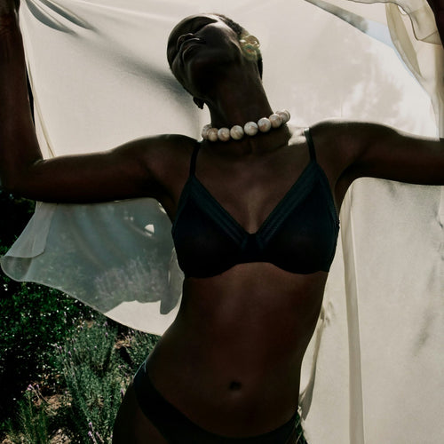 Person wearing a black bikini with a white fabric draped over them, standing outdoors.