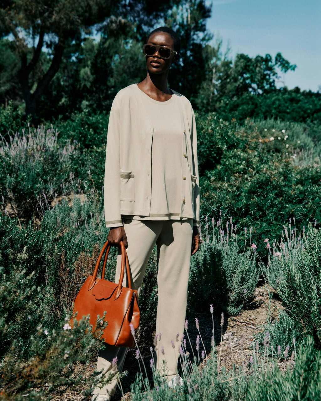 Woman holding an orange handbag in a garden setting