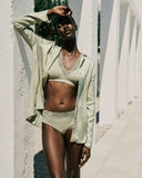 Woman in a light green bikini and cardigan standing against a white architectural background